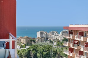 A high-rise building with multiple balconies, a view of the sea, and surrounding greenery.