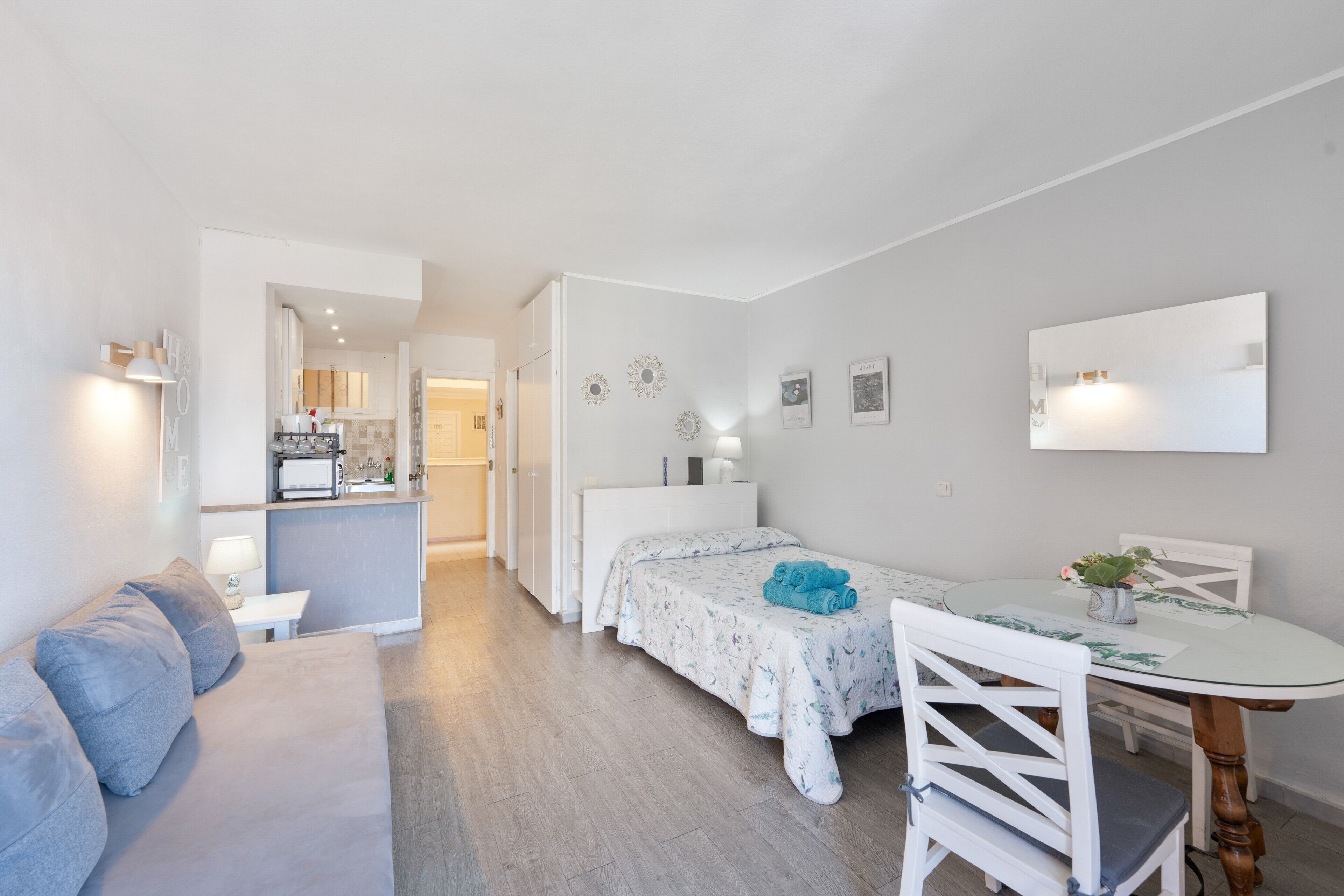 Een compacte kamer met een bed, een kleine eettafel met stoelen, een bank en een kitchenette achterin.