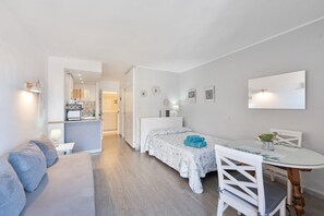 A compact room with a bed, a small dining table with chairs, a sofa, and a kitchenette in the background.