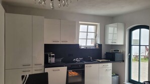 Eine moderne Küche mit weißen Schränken, einer schwarzen Arbeitsplatte und einem eingebauten Backofen. Über der Spüle befindet sich ein Fenster und eine Tür führt nach draußen.