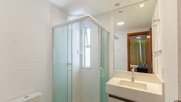 Un baño con cabina de ducha de vidrio, un lavamanos blanco y un espejo sobre él.