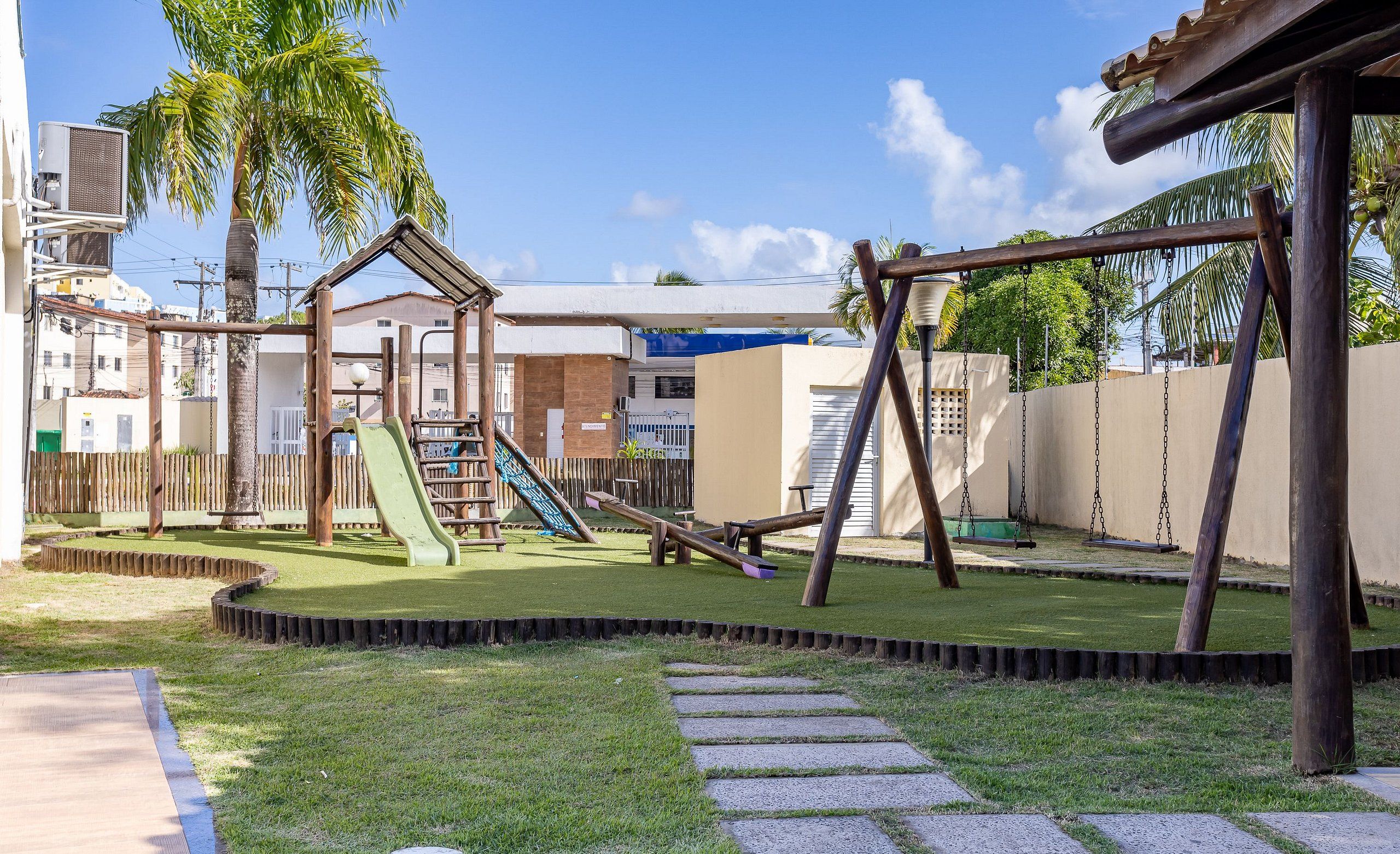 A playground with slides and swings, surrounded by a fence and palm trees.