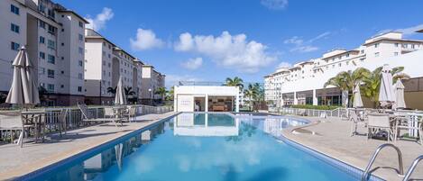 A swimming pool with lounge chairs and umbrellas, surrounded by multi-story buildings with balconies.