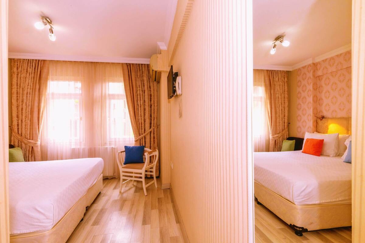 A hotel room with two beds, a chair, a bedside table, a lamp, and a telephone.