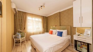 A hotel room with a large bed, a wooden chair, a minibar, and a window with curtains. - Walnut Shell Hotel Sultanahmet (Istanbul)