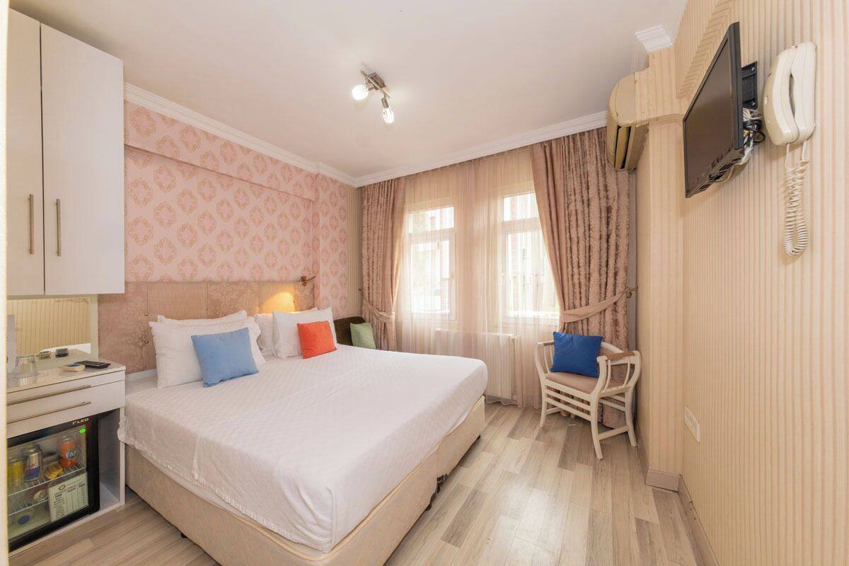 A hotel room with a large bed, a desk with a computer, a chair, and a TV mounted on the wall.