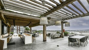 Una terraza en la azotea con pérgola, mobiliario exterior y vistas a la ciudad.