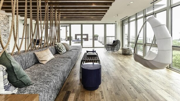 Un amplio salón con techo de madera, un sillón colgante, un sofá con cojines y un ventanal con vistas a la ciudad.
