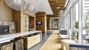 Un moderno vestíbulo de hotel con un mostrador de recepción de madera, una pantalla grande y una zona de estar con sillas de mimbre y una mesa redonda.