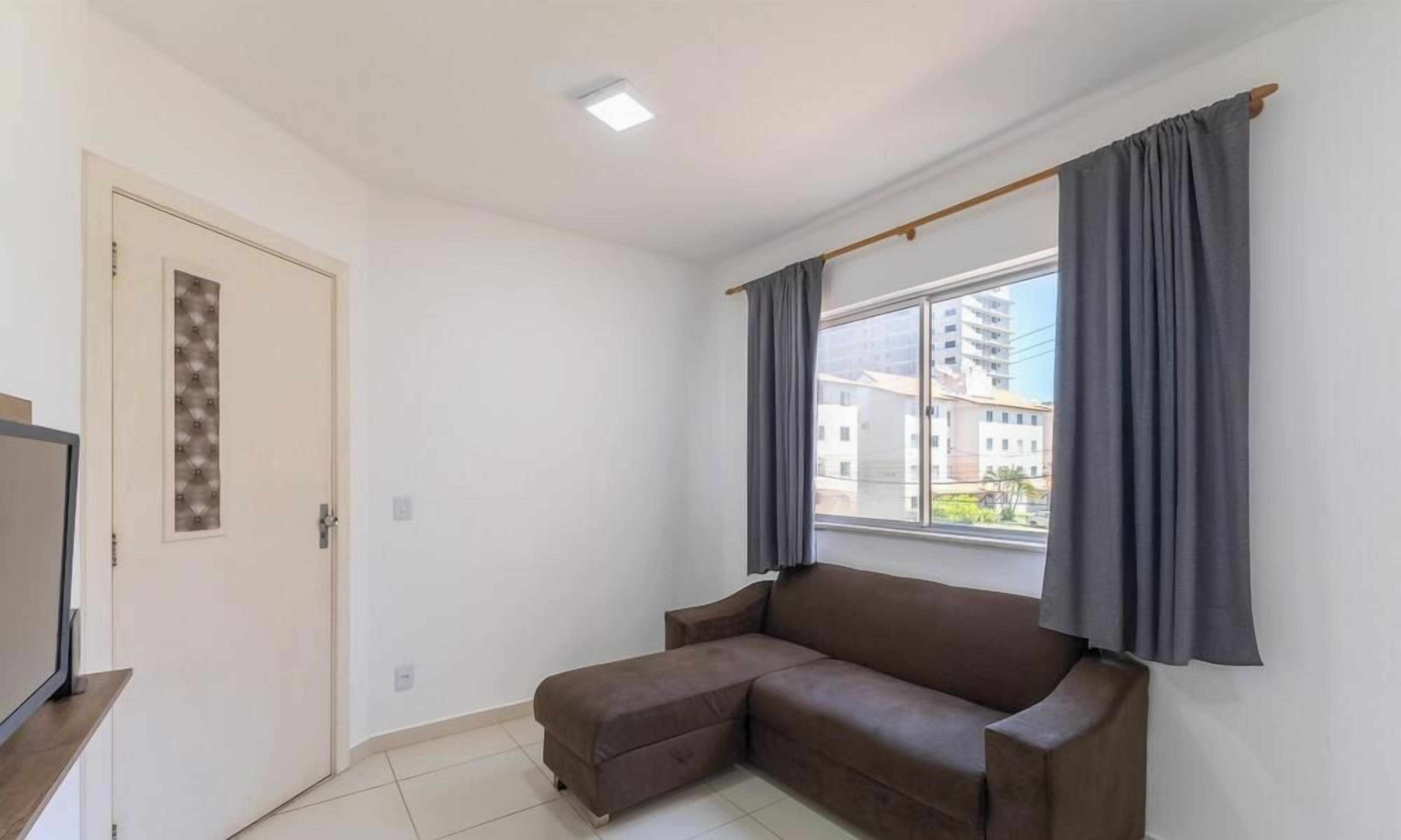 A room with a brown sofa, a window with curtains, a door with a decorative panel, and a television on a stand.