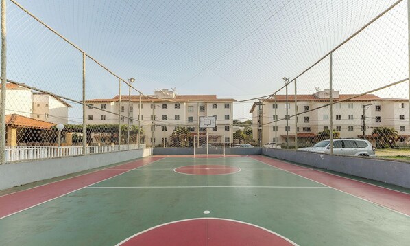 An outdoor basketball court enclosed by a chain-link fence with buildings in the background. - Apartment w/ Pool 350m From the Beach Vjgm0102 (Ilhéus)