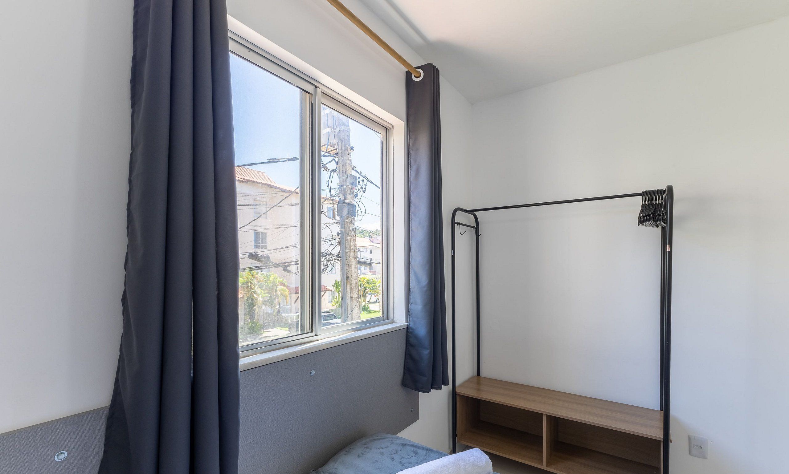 A room with a bed, a window with curtains, a wooden shelf, and a metal rack.