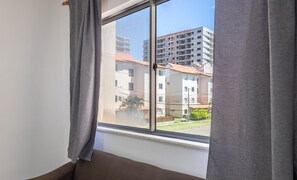 A room with a large window, a brown sofa, and a view of a residential area with buildings and a clear sky.
