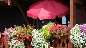 A wooden building with a red umbrella and flower planters. - Panorama Apartment 2 – NEW! incl. 3 Worlds Card – 140 Free Attractions (Bernau im Schwarzwald)