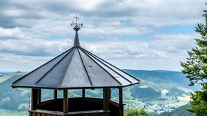 A wooden observation tower with a metal roof and a weather vane, surrounded by greenery and overlooking a valley. - Panorama Apartment 2 – NEW! incl. 3 Worlds Card – 140 Free Attractions (Bernau im Schwarzwald)