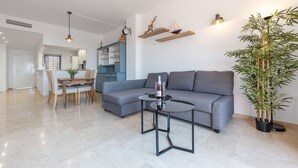 A modern living room with a grey sofa, a round black coffee table, and a dining area with wooden chairs.