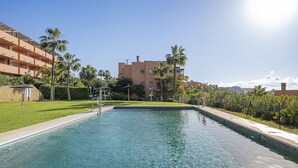 A swimming pool with clear water, surrounded by a well-maintained lawn and palm trees.