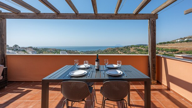 A wooden pergola with a table set for two, overlooking a scenic landscape.