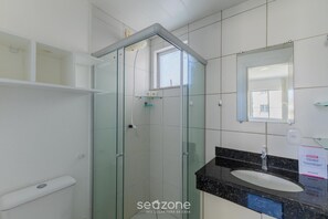 A bathroom with a glass-enclosed shower, a white sink, and a mirror above it.