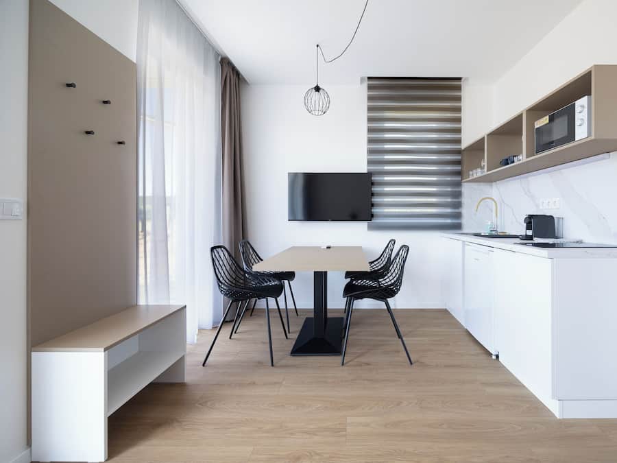 A modern kitchen with a dining area, white cabinetry, a flat-screen TV, and a built-in microwave.
