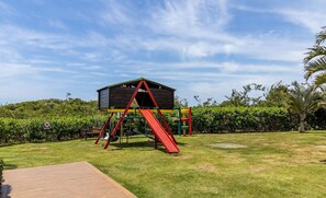 A playground with a slide and climbing structure, surrounded by a grassy area and a wooden deck.