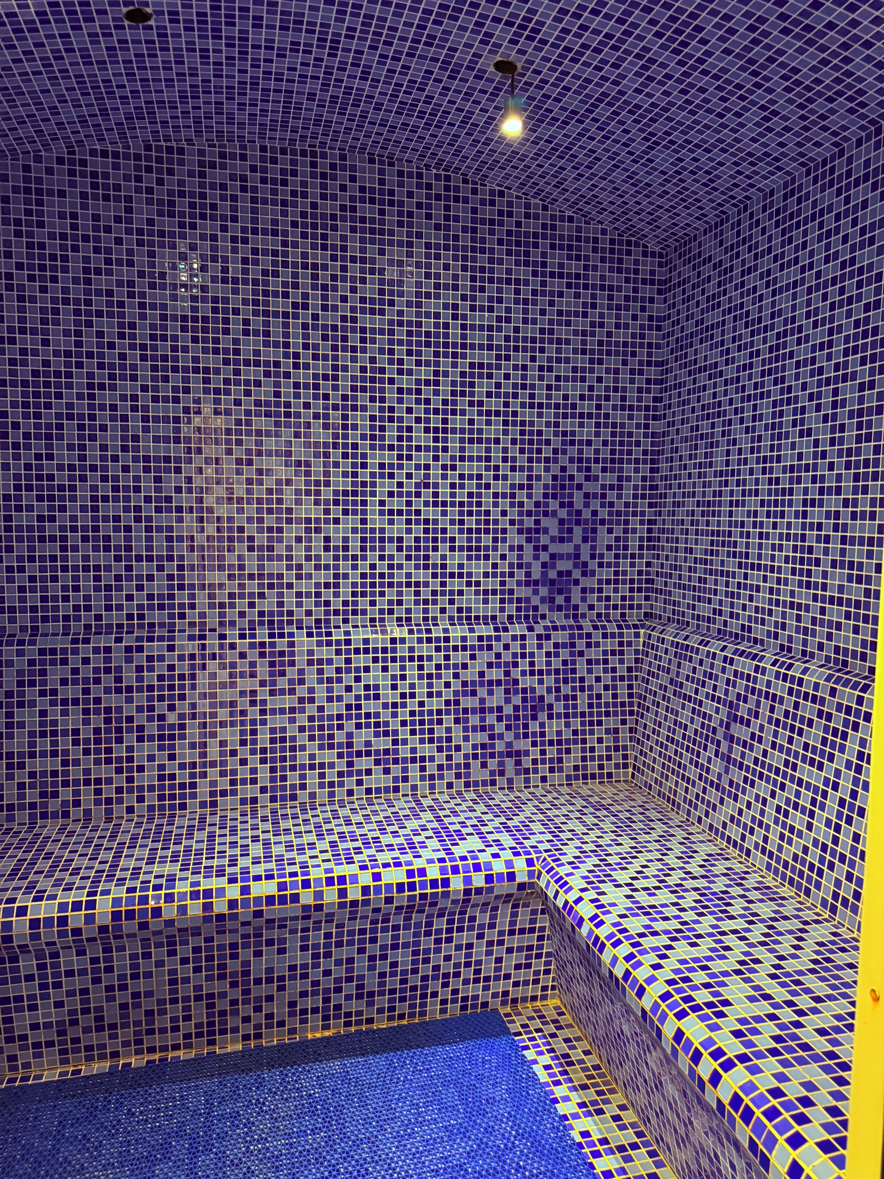 Une pièce dont le sol et les murs sont recouverts de carreaux, avec un banc et un luminaire au plafond.