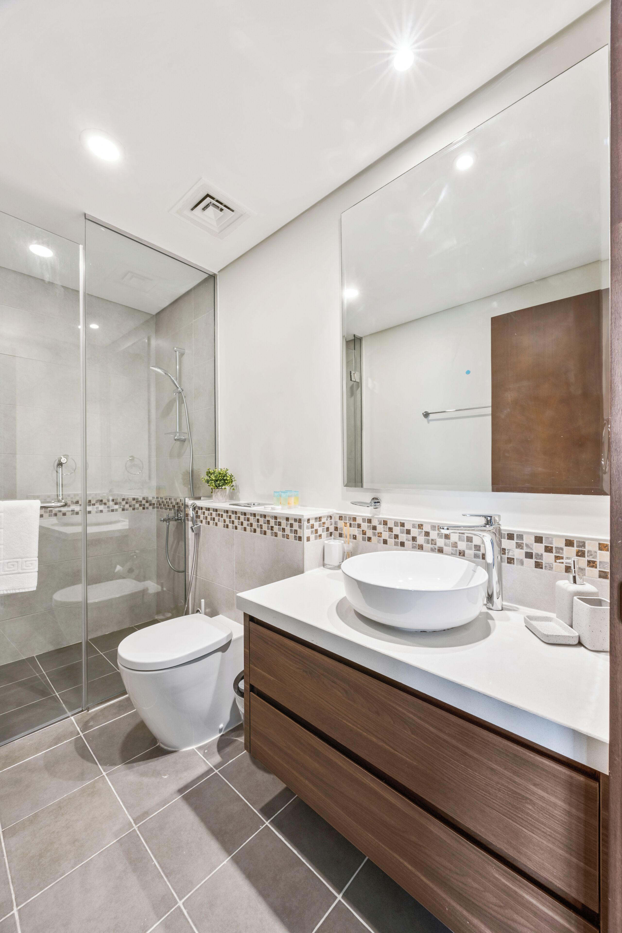 Un bagno moderno con doccia vetrata, lavandino bianco e mobile contenitore in legno.