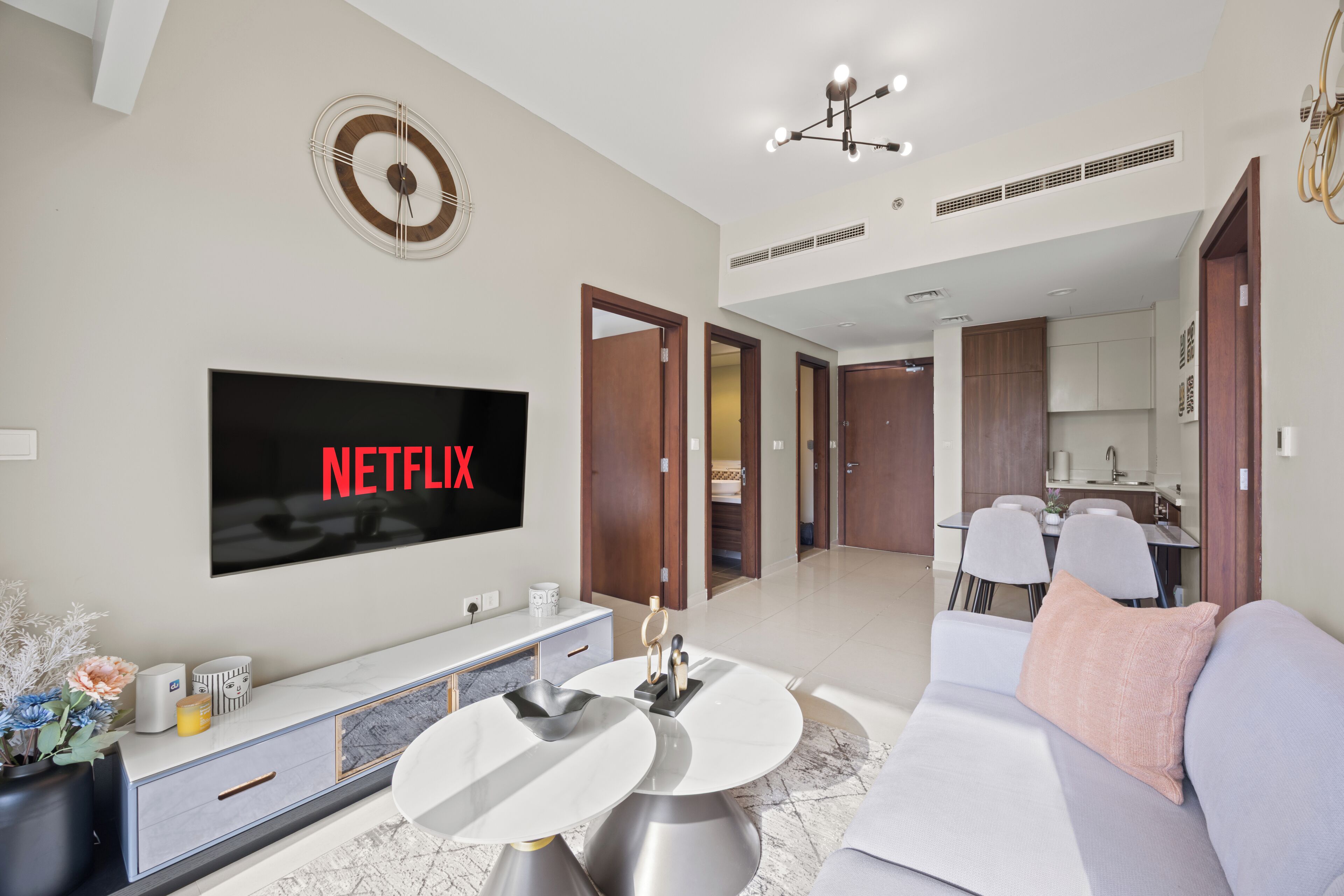 Un salon moderne avec un téléviseur à écran plat, un canapé, une table basse et un coin repas à l’arrière-plan.
