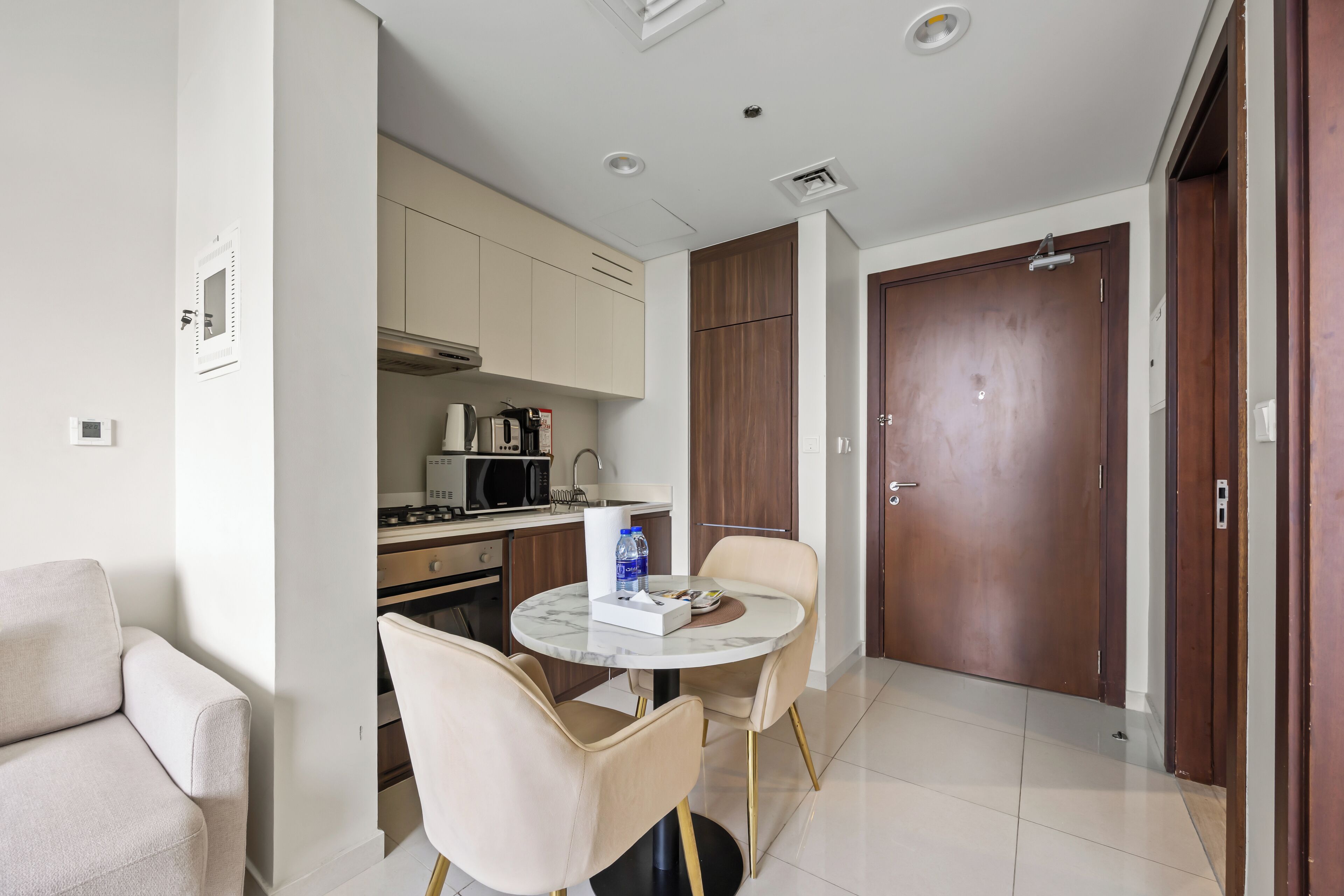 A modern kitchen with a dining area, including a round table with chairs, a sofa, and a wooden door.