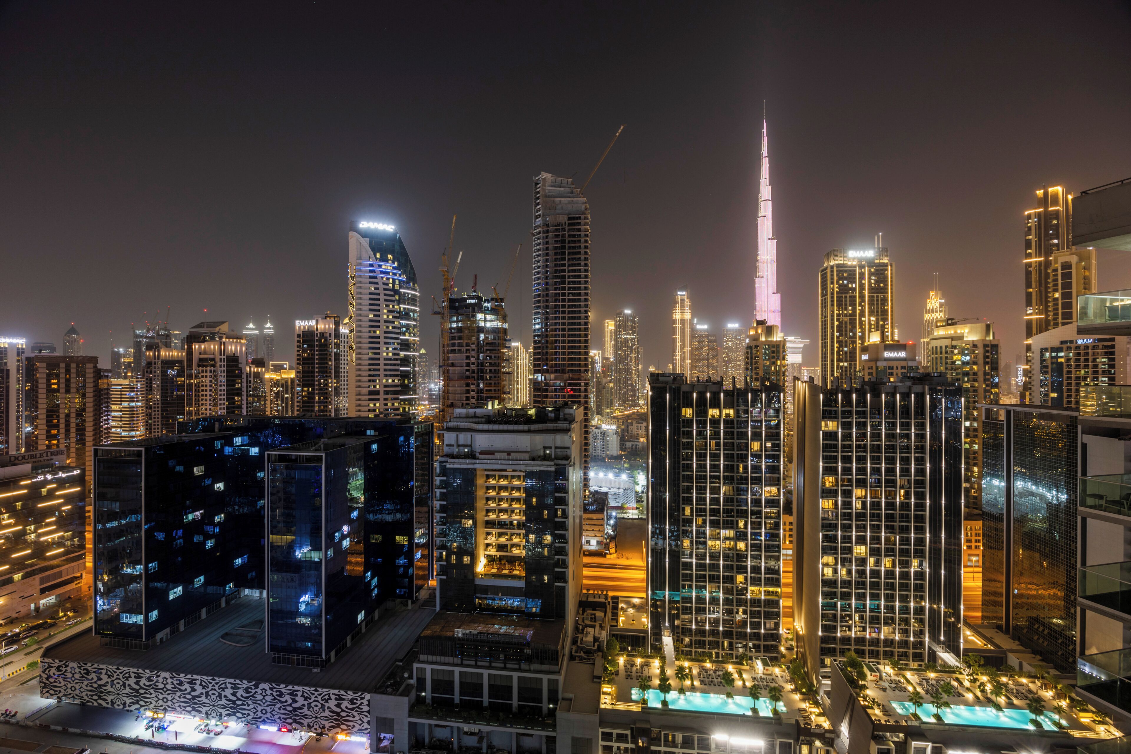 A high-rise hotel with multiple floors, a rooftop pool, and a view of the city skyline at night.