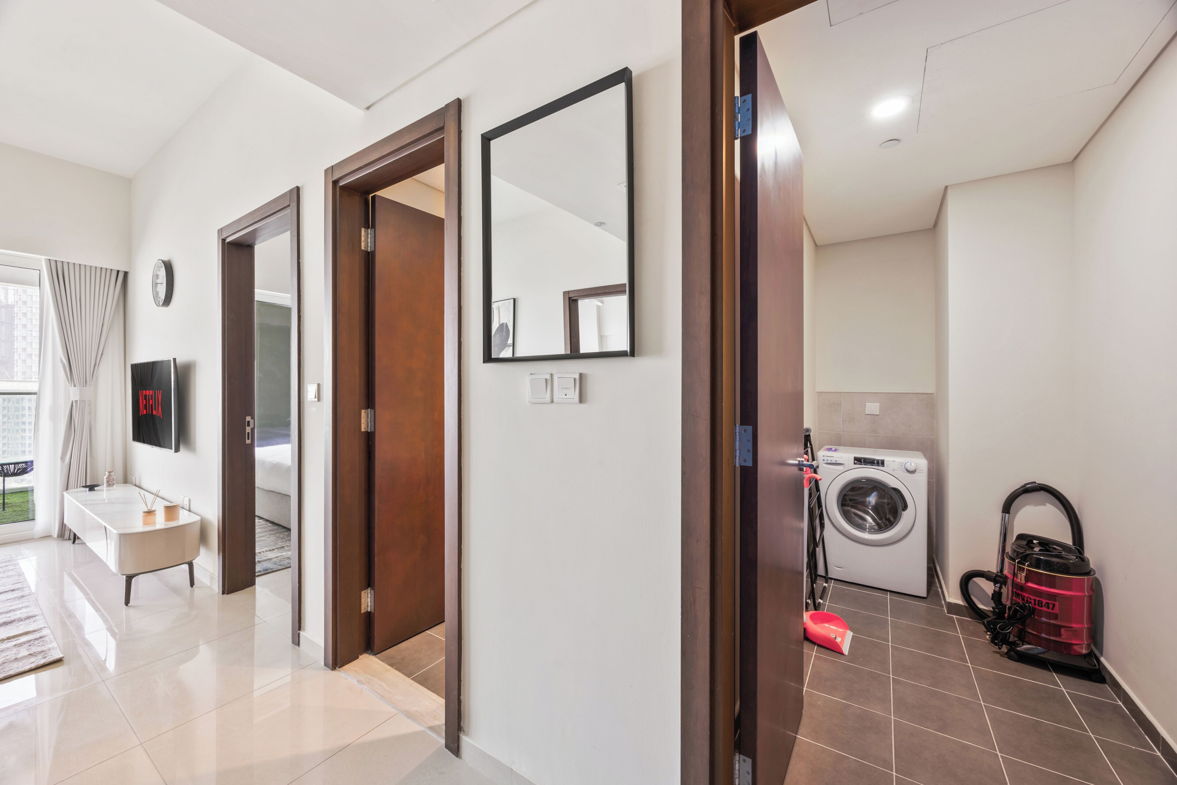 A hotel room with a large mirror, a washing machine, and a vacuum cleaner.