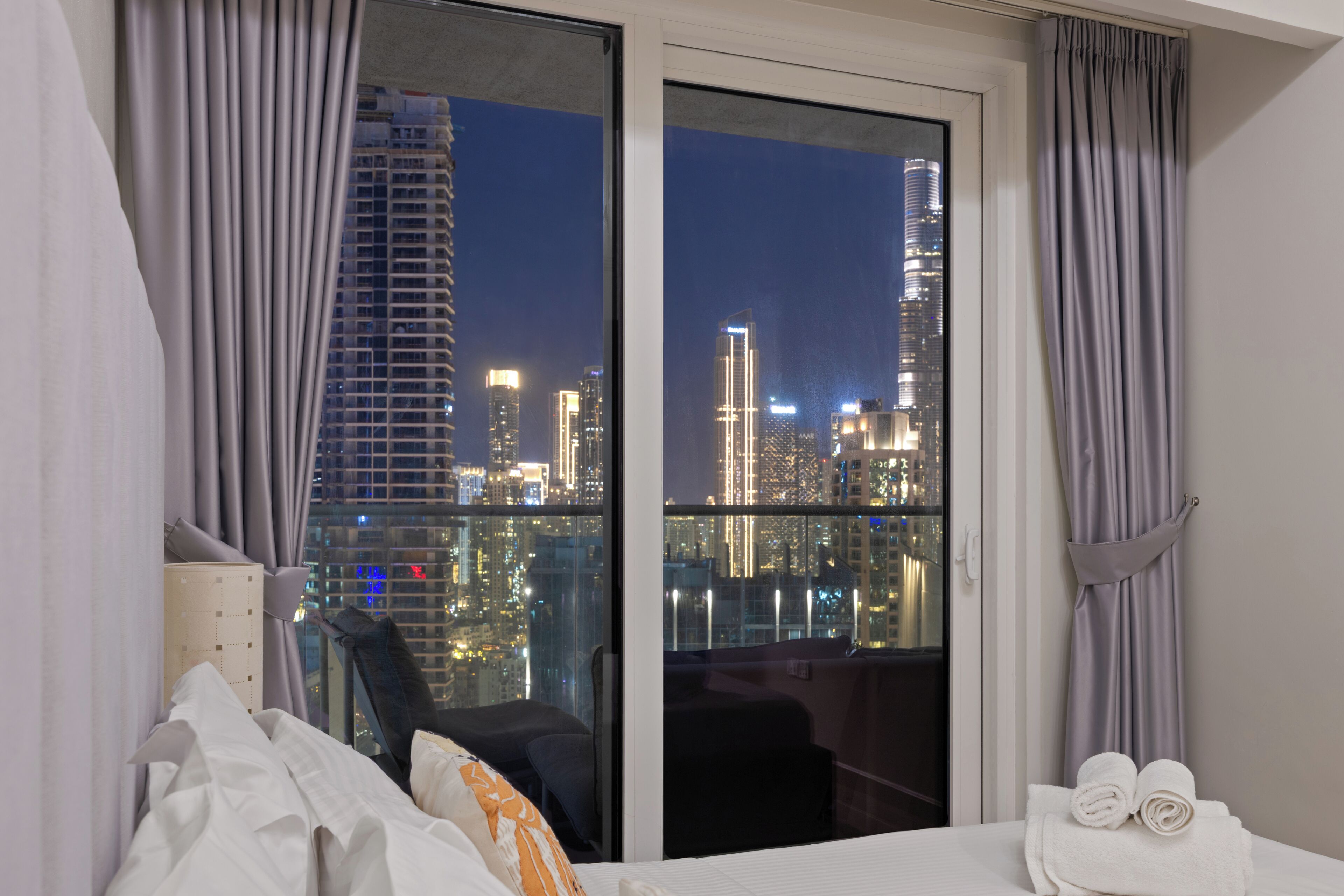 Ein Hotelzimmer mit großem Fenster und Blick auf die nächtliche Skyline.