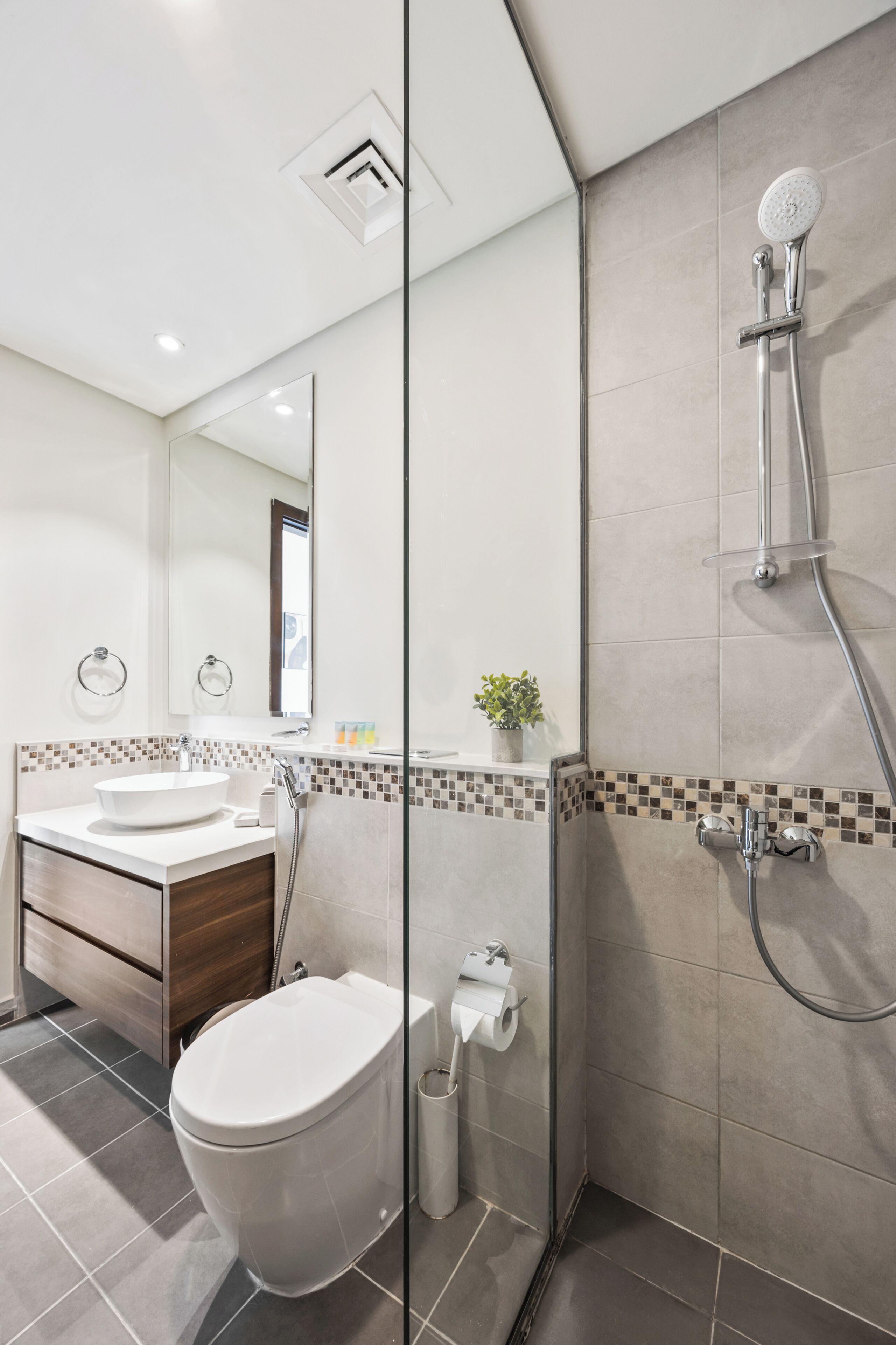Een moderne badkamer met een glazen douchecabine, een wit wastafelmeubel en een toilet.