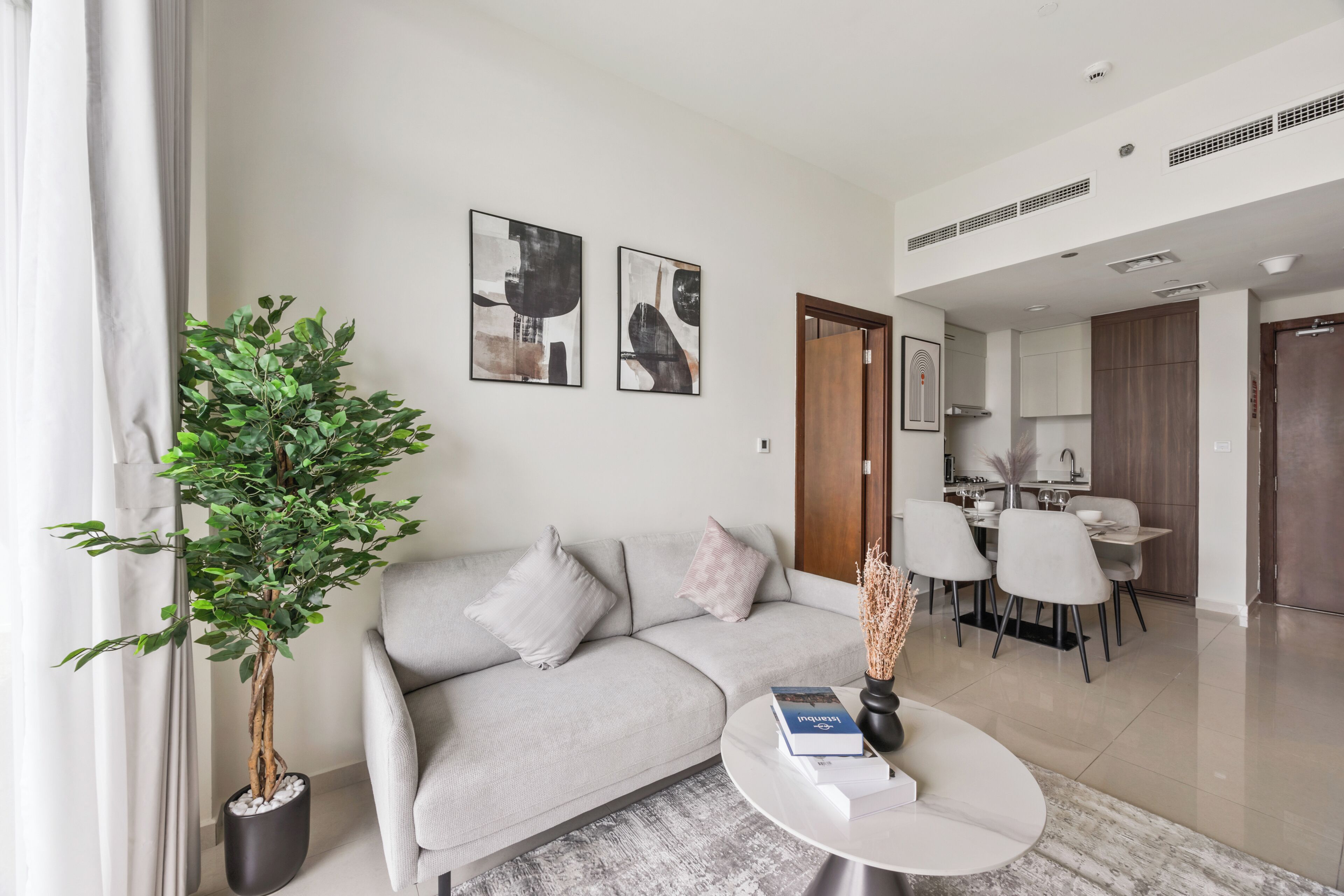 Ein modernes Wohnzimmer mit einem grauen Sofa, einem Couchtisch mit Büchern, einer Topfpflanze und abstrakter Wandkunst.