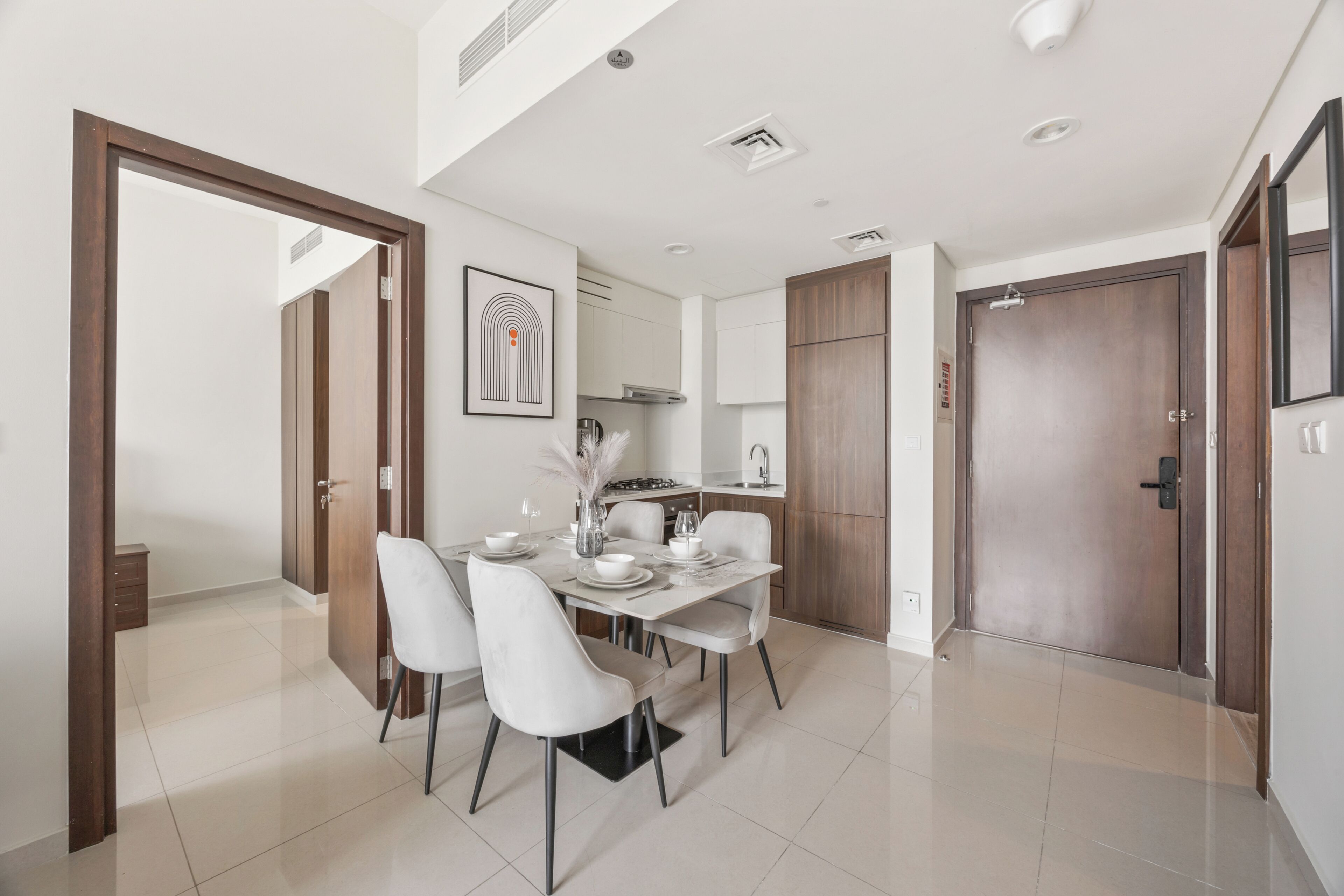 A modern dining area with a white table set for four, surrounded by white chairs.