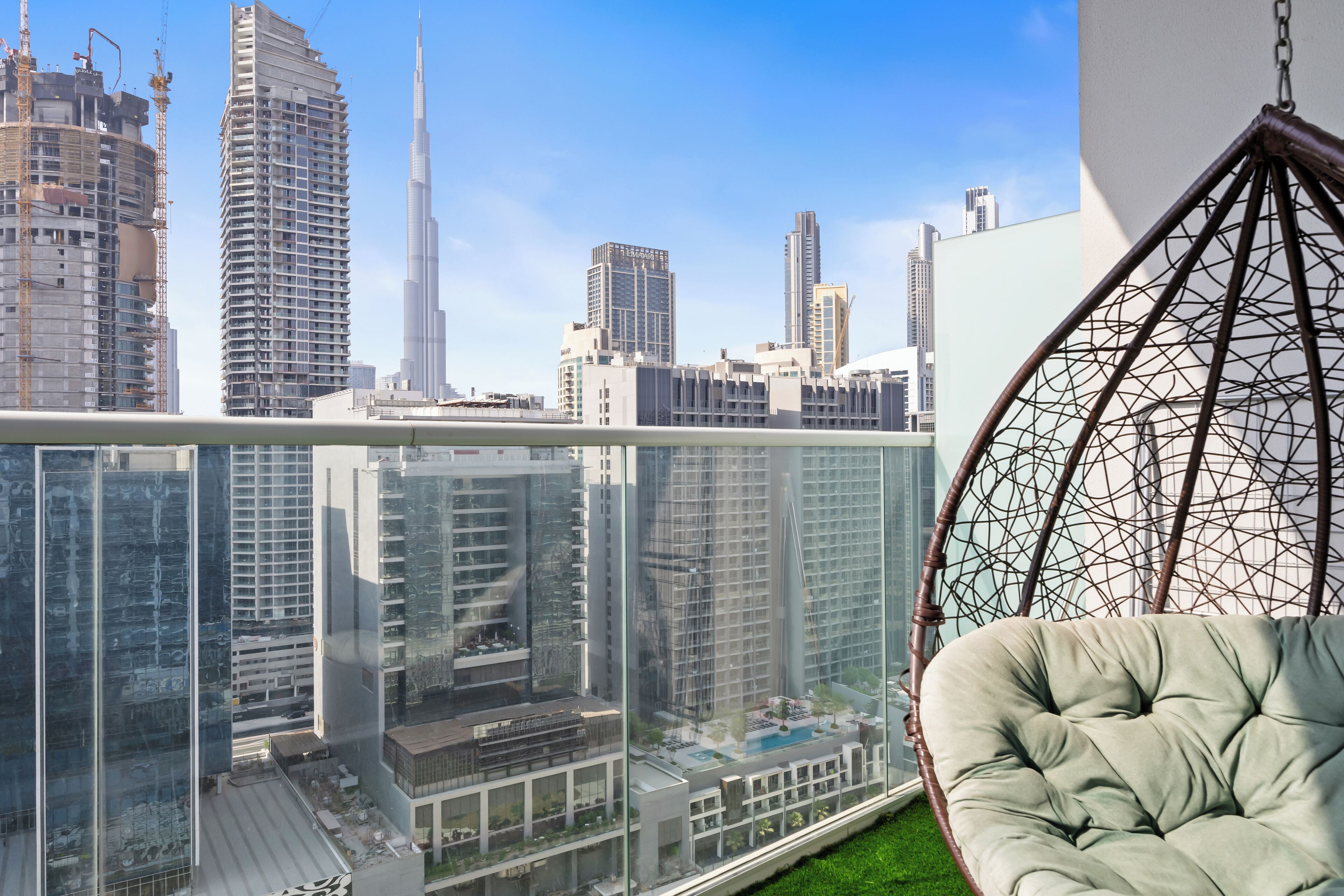 Een balkon met een hangstoel, uitzicht op moderne wolkenkrabbers en een glazen balustrade.