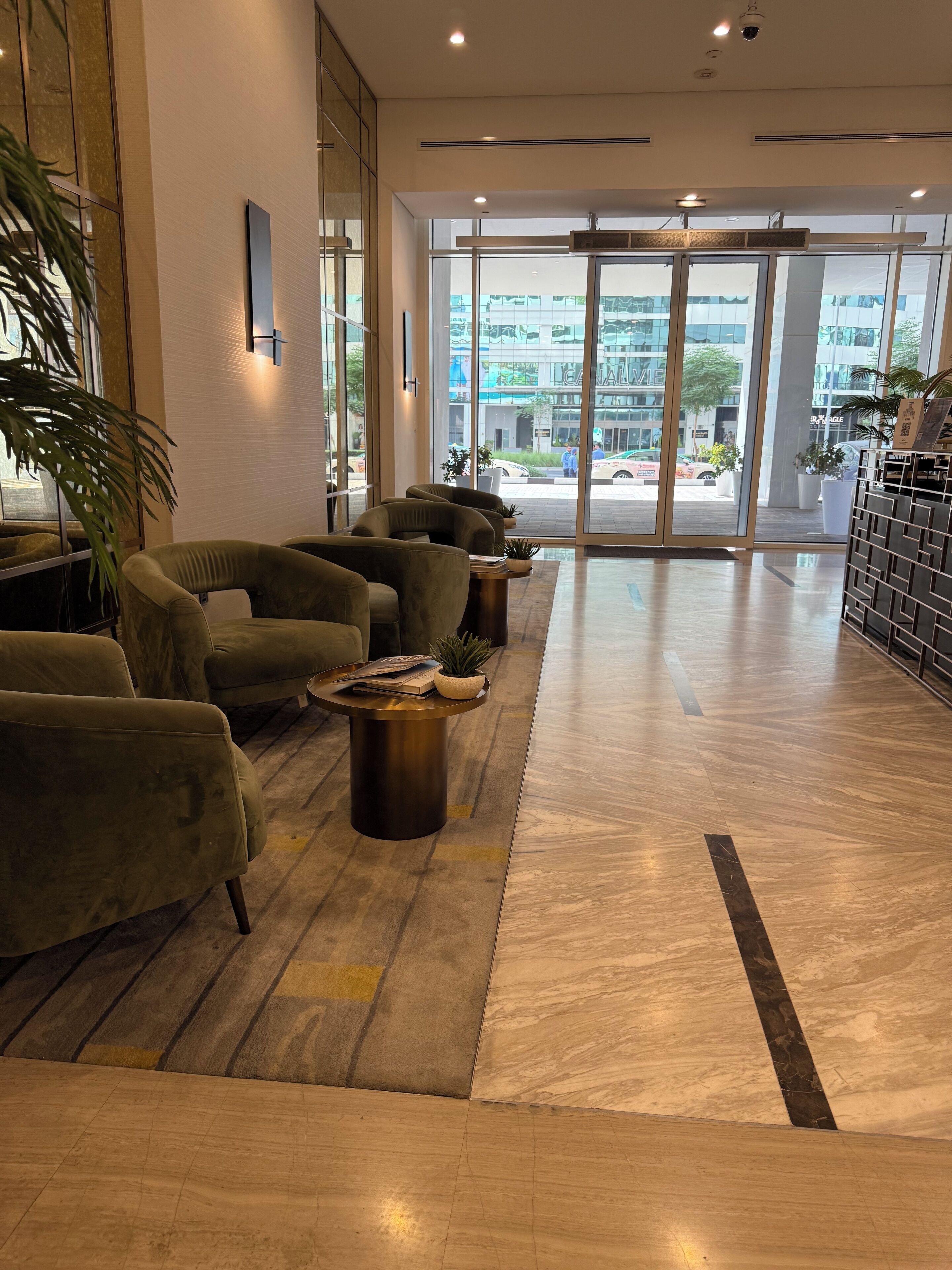 A modern lobby with seating, a reception desk, and large windows offering a view of the street.