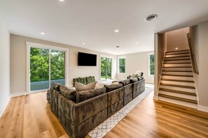A spacious living room with a large sectional sofa, a flat-screen TV mounted on the wall, and a staircase leading to an upper level.