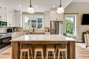 A modern kitchen with white cabinetry, a large island with stools, stainless steel appliances, and a view of a residential area.