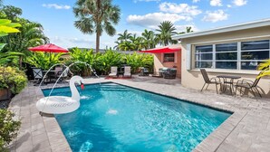 A swimming pool with a swan float, surrounded by palm trees and outdoor seating. - Oasis Backyard with Heated Pool! | Oakland Park (Wilton Manors)