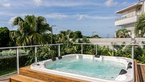 A hot tub on a wooden deck with a view of a modern building and lush greenery. - Apartment in Thai Beach Home Spa Tbs1105 (Florianópolis)