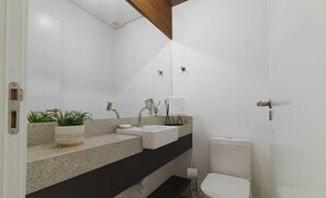 Un baño moderno con encimera de granito, un lavamanos blanco, inodoro y planta en maceta.
