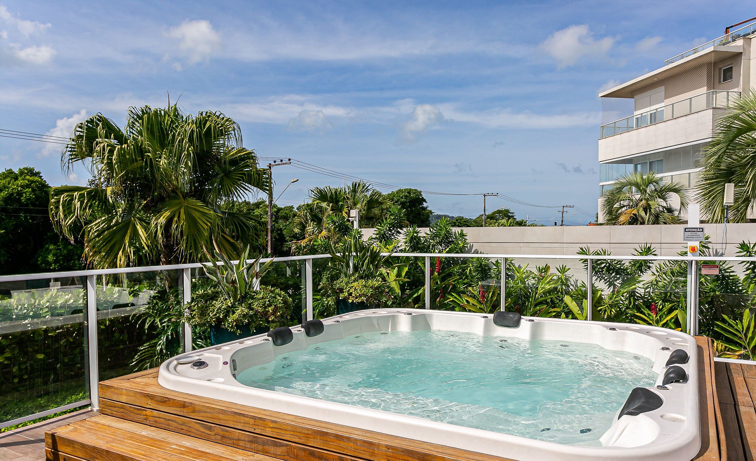 Un jacuzzi en una terraza de madera con vistas a un edificio moderno y abundante vegetación.