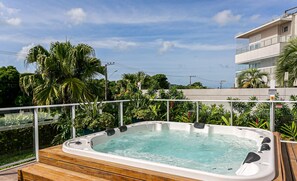 Un jacuzzi en una terraza de madera con vistas a un edificio moderno y abundante vegetación.