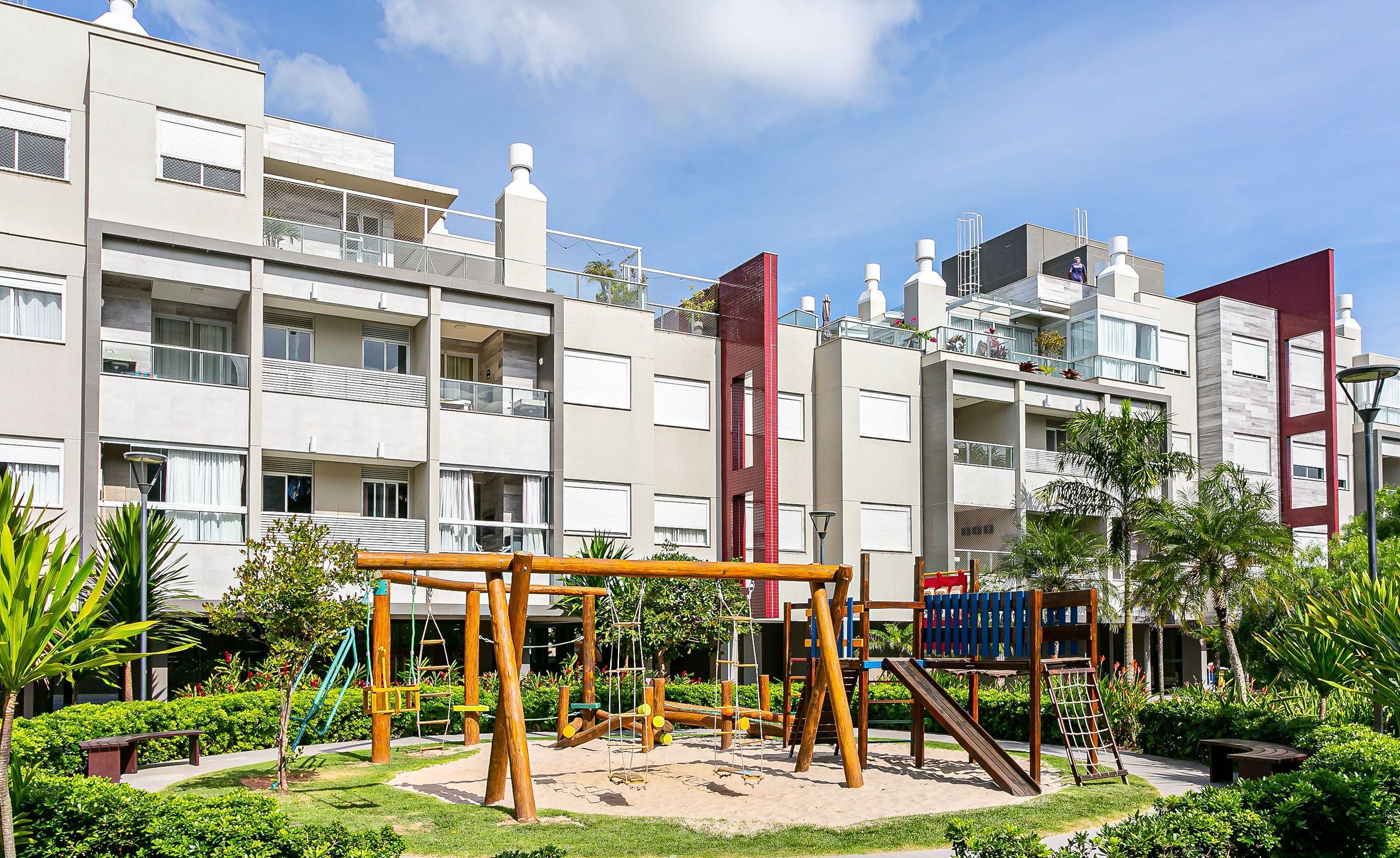 A playground area with swings and slides, surrounded by well-maintained greenery and modern buildings in the background.