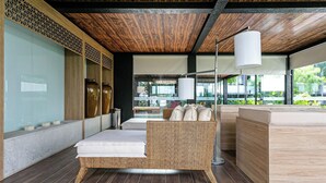 A modern lounge area with a wicker sofa, a white lamp, and a view of the outdoors. - Apart in Thai Beach Home Spa Cond sea Front Tbs106 (Florianópolis)