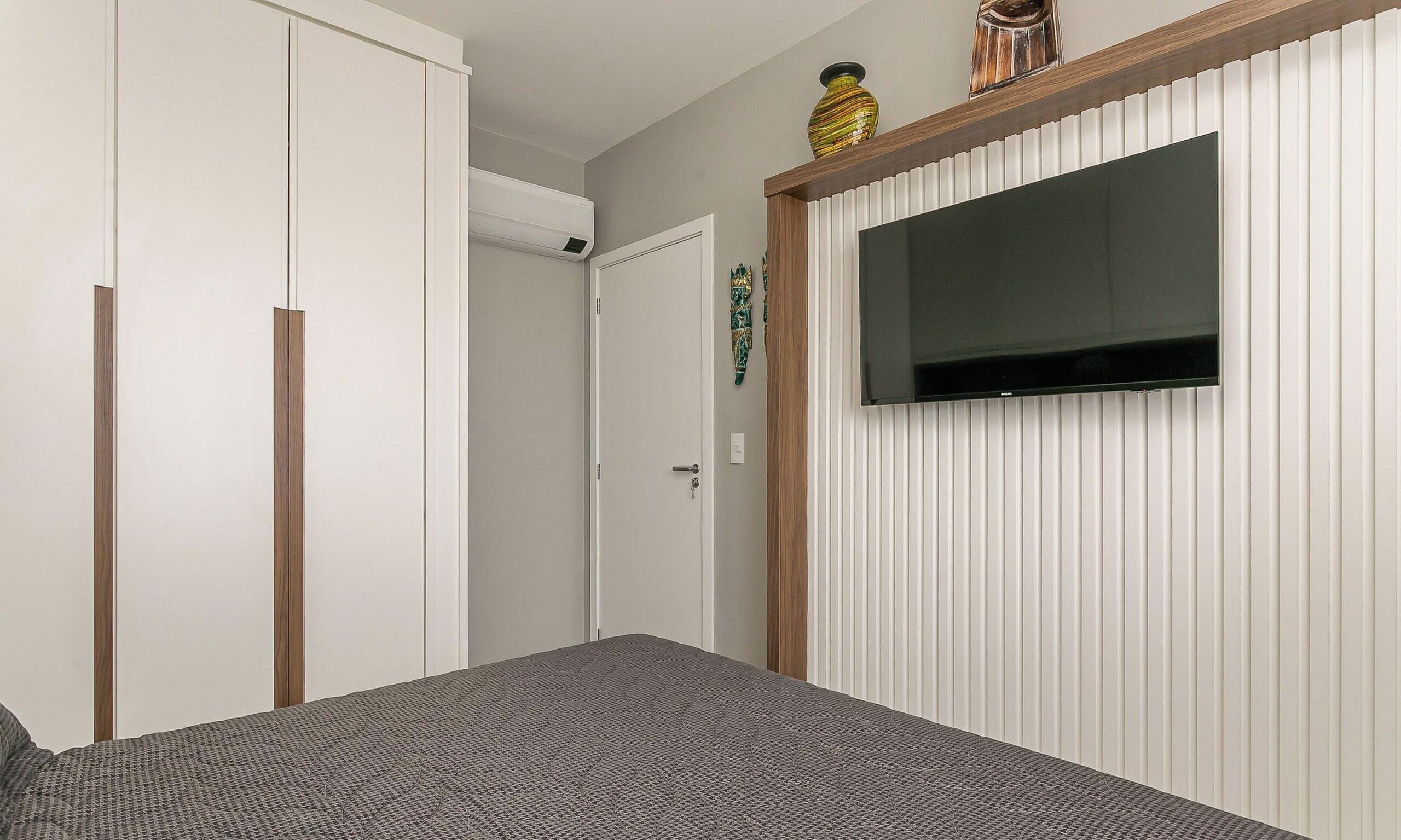 Un dormitorio con una cama, un armario, un televisor montado en la pared y una puerta decorada.