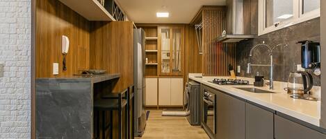 A modern kitchen with a built-in stove, a coffee maker, and a microwave. There is a wooden cabinet and a countertop.
