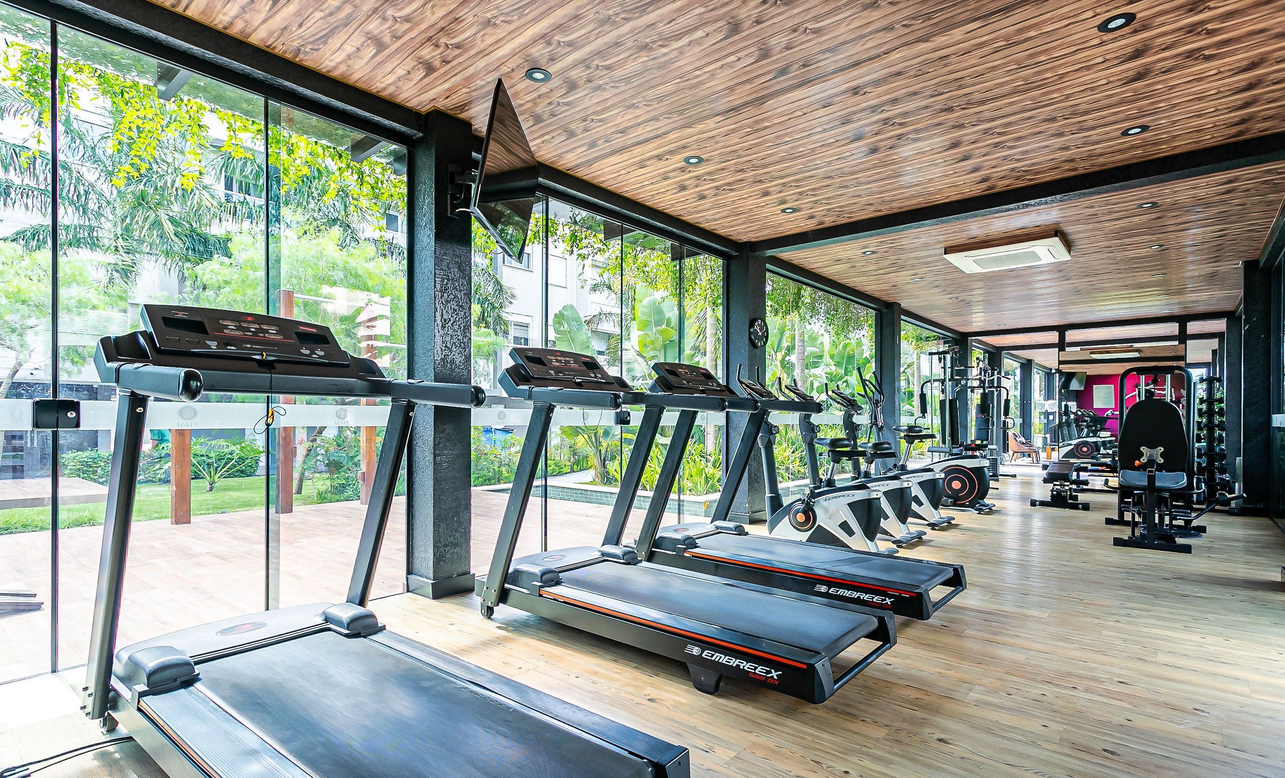 Un gimnasio con cintas de correr, máquinas de pesas y un amplio ventanal con vistas a zonas verdes.
