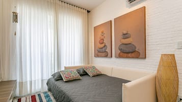 Un dormitorio con cama, cortinas, aire acondicionado de pared y dos cuadros.